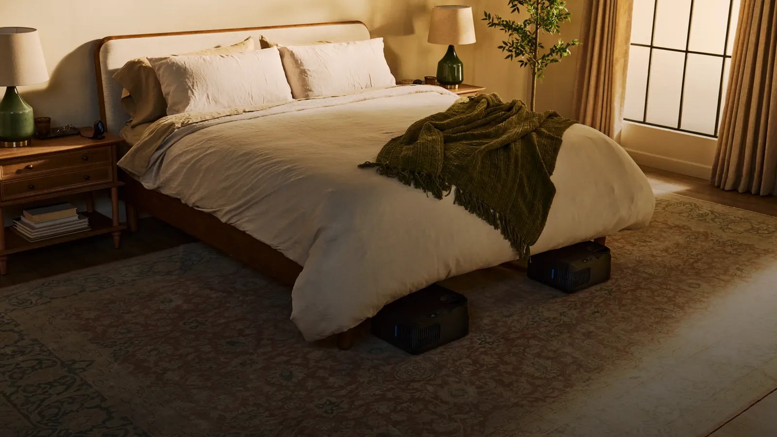 A made bed in a warm, lamp-lit bedroom with two Chilipad docks on the rug beneath it, one for each side